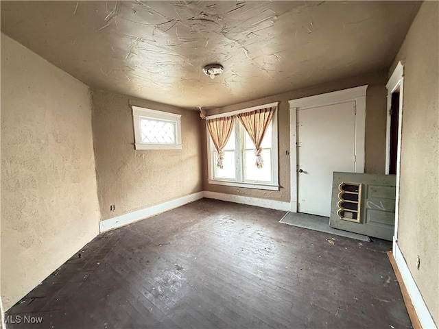 unfurnished living room featuring baseboards, wood finished floors, and a textured wall