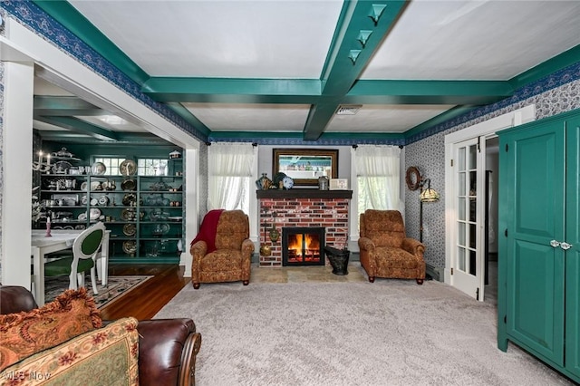 living area featuring a brick fireplace, coffered ceiling, plenty of natural light, and wallpapered walls