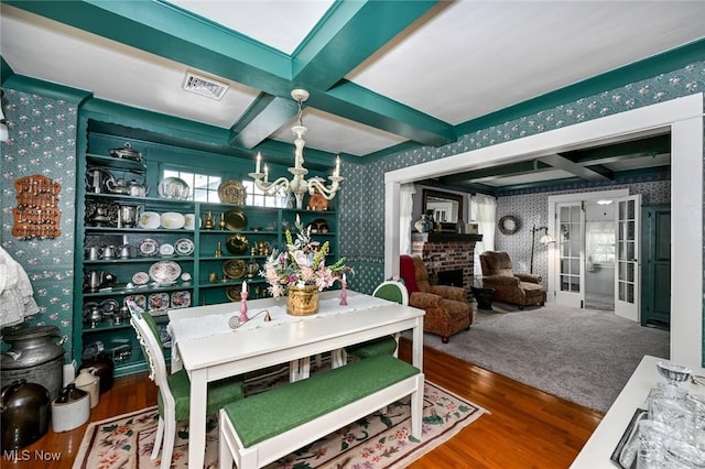 dining room with wallpapered walls, visible vents, coffered ceiling, wood finished floors, and beam ceiling