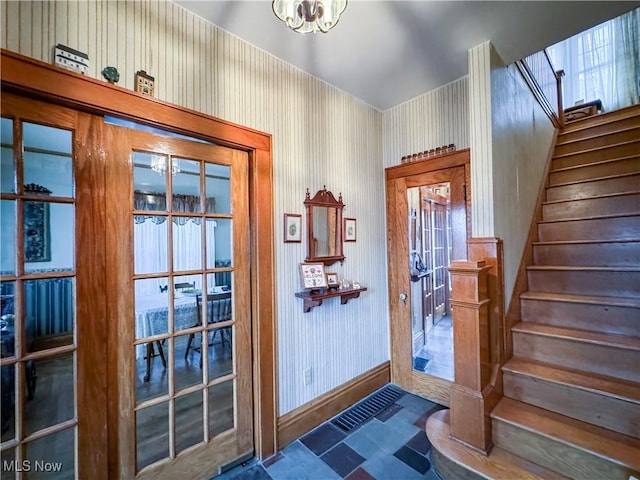 doorway to outside with wallpapered walls, baseboards, stairway, and a chandelier