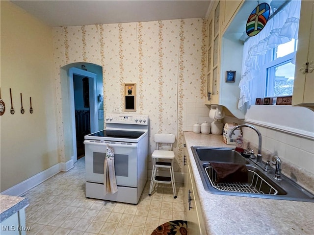 kitchen with wallpapered walls, tasteful backsplash, white range with electric stovetop, baseboards, and a sink