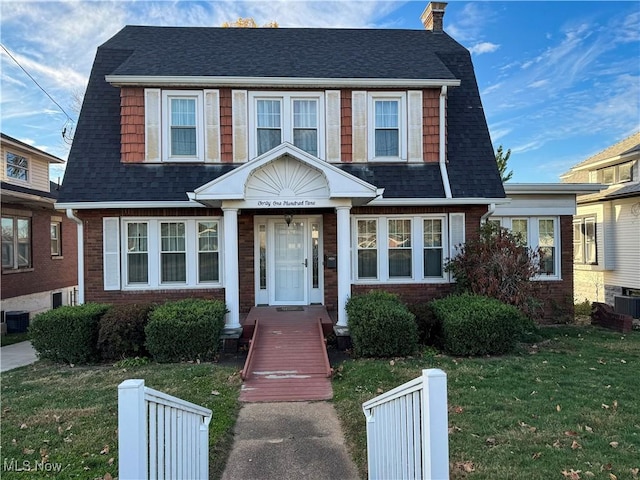 dutch colonial with a shingled roof, a front yard, cooling unit, and brick siding