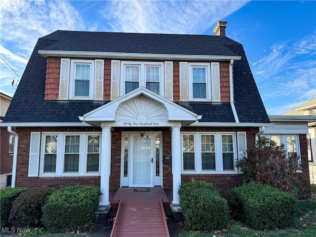 colonial inspired home featuring roof with shingles, a chimney, and brick siding