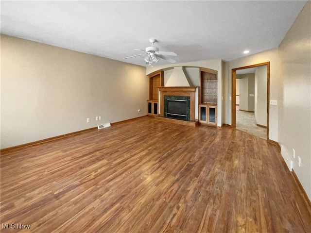 unfurnished living room featuring visible vents, a fireplace with raised hearth, ceiling fan, wood finished floors, and baseboards