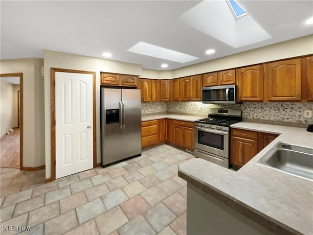 kitchen with stainless steel appliances, tasteful backsplash, light countertops, brown cabinetry, and a sink