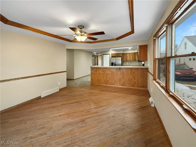 unfurnished living room with baseboards, visible vents, ceiling fan, and light wood finished floors