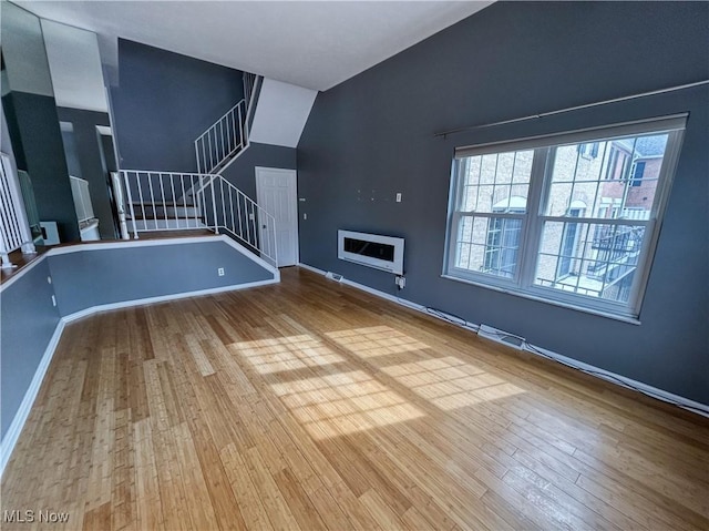 unfurnished living room featuring stairs, wood finished floors, lofted ceiling, and baseboards