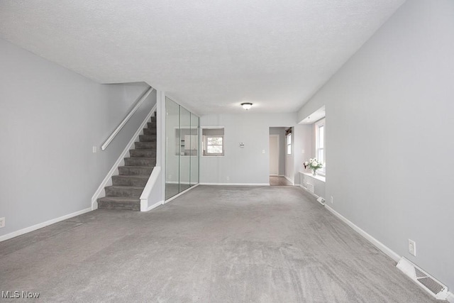 unfurnished living room featuring a wealth of natural light, visible vents, carpet flooring, and stairs