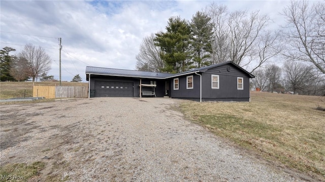 ranch-style house featuring gravel driveway, an attached garage, fence, metal roof, and a front lawn