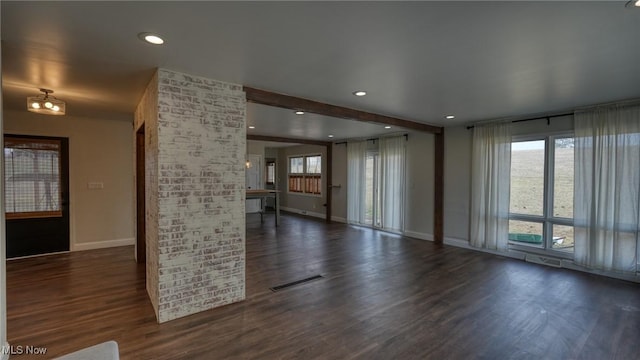 unfurnished living room featuring a wealth of natural light, dark wood-type flooring, visible vents, and baseboards