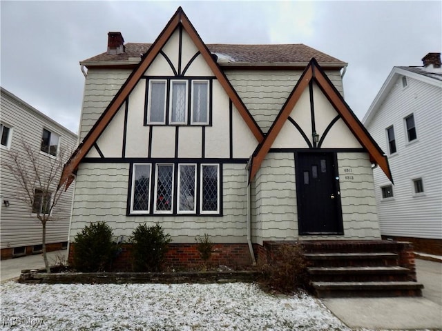 tudor house featuring entry steps, roof with shingles, and a chimney