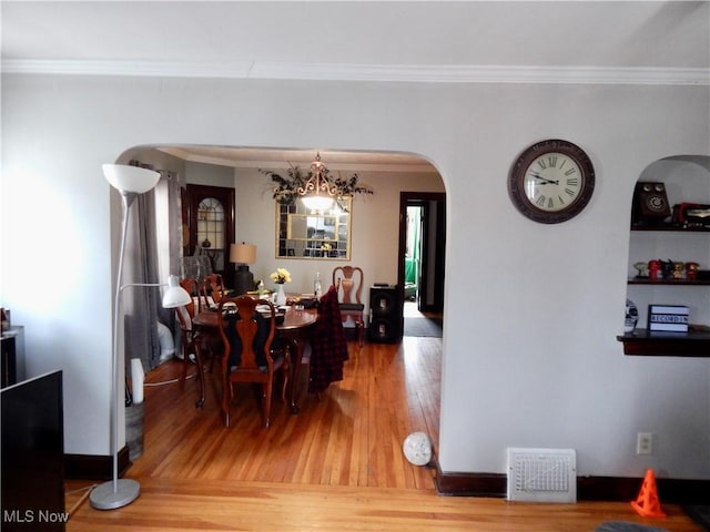 dining room featuring arched walkways, ornamental molding, wood finished floors, and visible vents