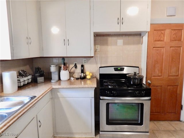 kitchen featuring gas stove, white cabinets, and backsplash