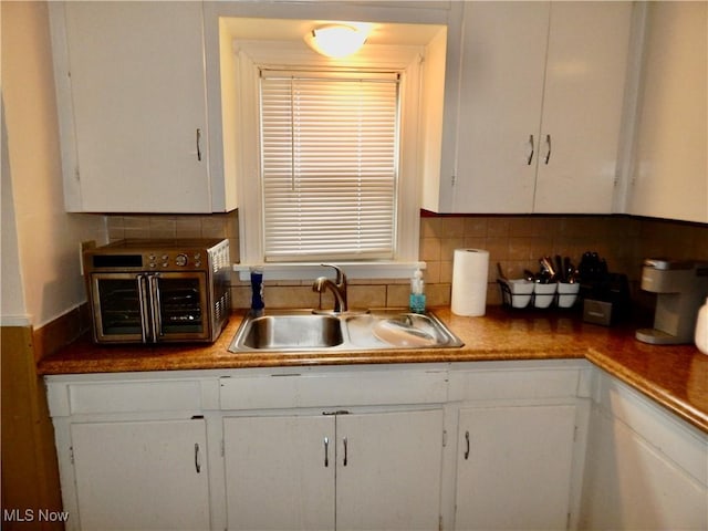 kitchen with a toaster, decorative backsplash, white cabinets, and a sink