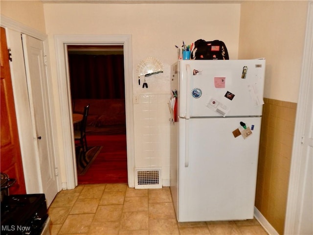 kitchen featuring tile walls, visible vents, freestanding refrigerator, wainscoting, and light tile patterned flooring