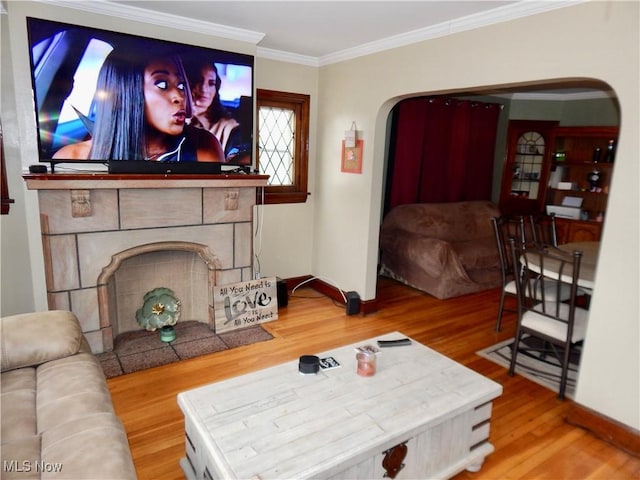 living area with arched walkways, a fireplace with flush hearth, wood finished floors, baseboards, and crown molding