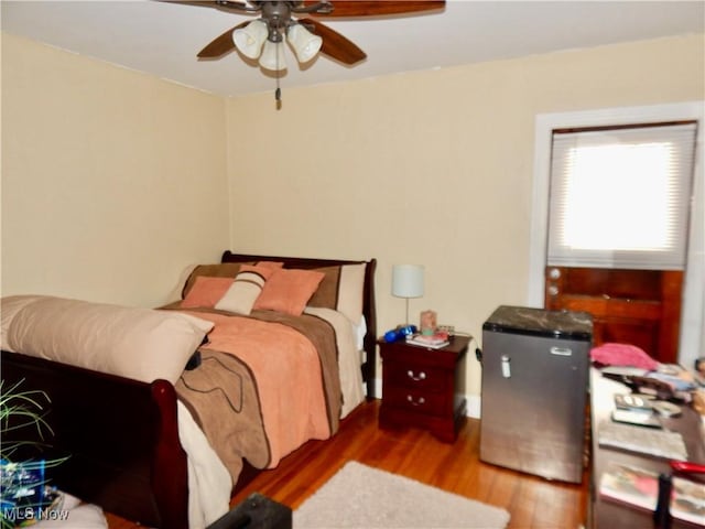 bedroom featuring a ceiling fan, wood finished floors, and fridge