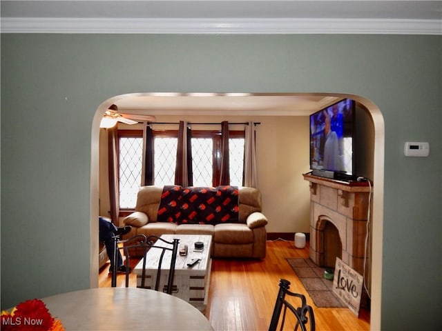 living area featuring a fireplace, arched walkways, wood finished floors, and ornamental molding