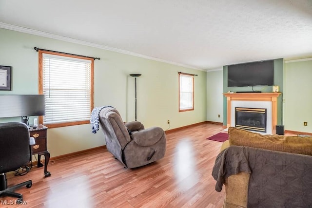 living area with a glass covered fireplace, crown molding, light wood-style flooring, and baseboards