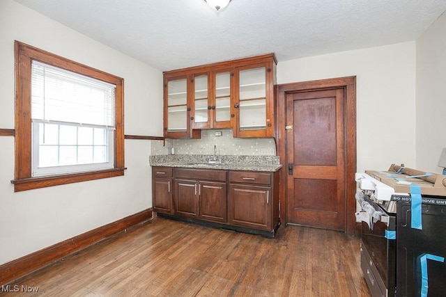 kitchen featuring stainless steel stove, baseboards, decorative backsplash, dark wood-style floors, and glass insert cabinets