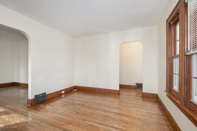 spare room with arched walkways, wood finished floors, visible vents, and baseboards