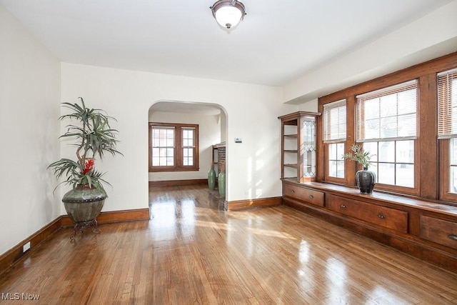 unfurnished room featuring baseboards, arched walkways, and wood finished floors