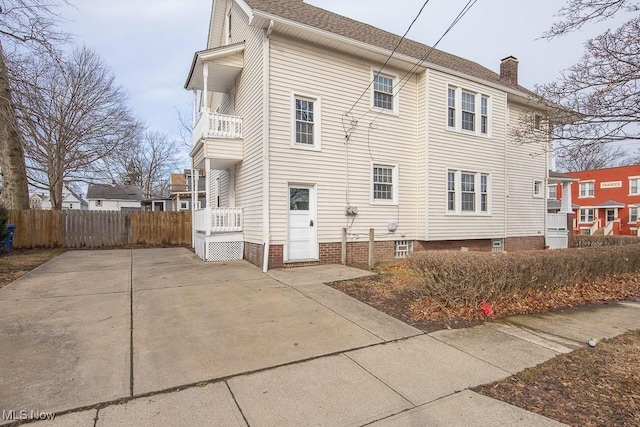 view of home's exterior featuring a balcony, a chimney, and fence