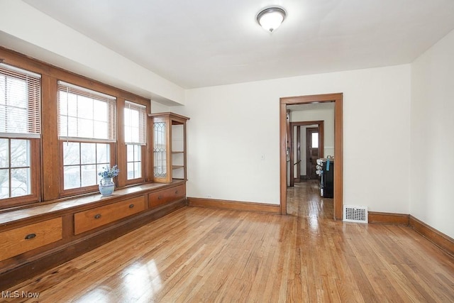 empty room featuring light wood-type flooring, visible vents, and baseboards