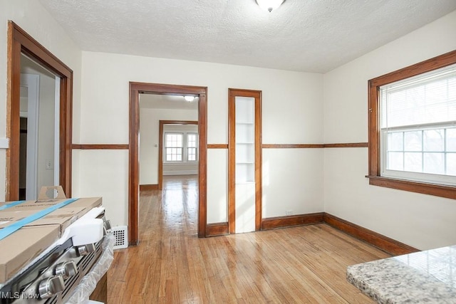 interior space featuring baseboards, a textured ceiling, and light wood finished floors