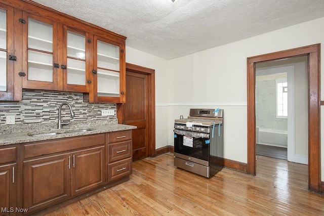 kitchen featuring stainless steel gas stove, tasteful backsplash, light stone counters, light wood-type flooring, and a sink