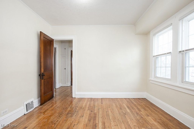 spare room with light wood finished floors, baseboards, visible vents, and ornamental molding