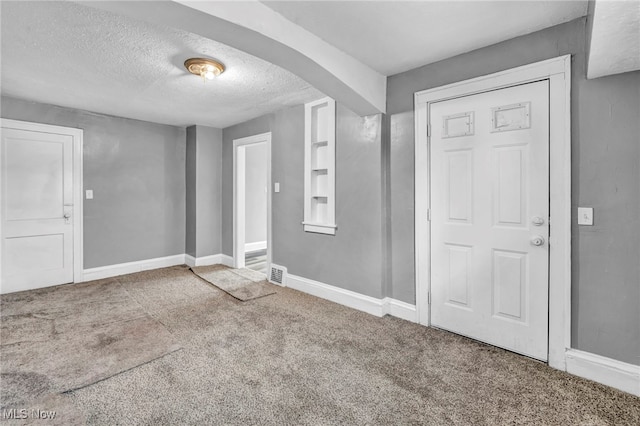 foyer with baseboards, a textured ceiling, arched walkways, and carpet flooring