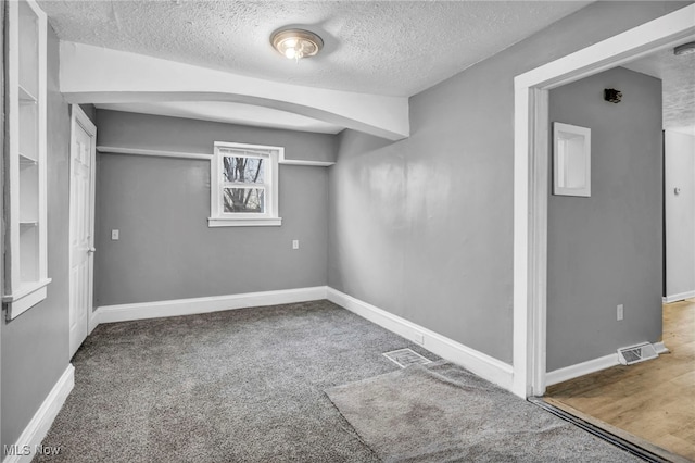 basement featuring arched walkways, carpet, a textured ceiling, and baseboards