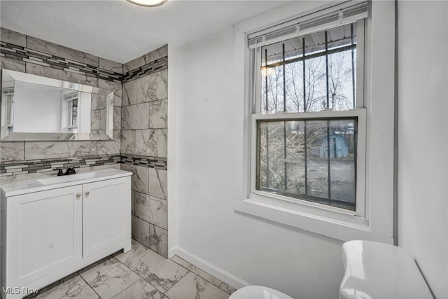 bathroom featuring toilet, marble finish floor, a textured ceiling, vanity, and tile walls