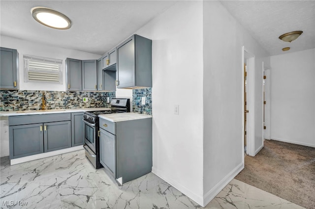 kitchen with baseboards, gas range, a sink, marble finish floor, and backsplash