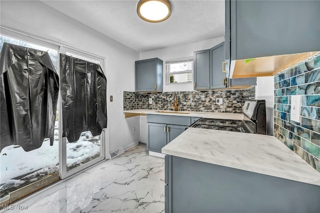 kitchen with gray cabinetry, a sink, marble finish floor, decorative backsplash, and gas stove