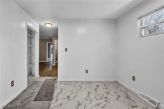 spare room with marble finish floor, baseboards, visible vents, and a textured ceiling