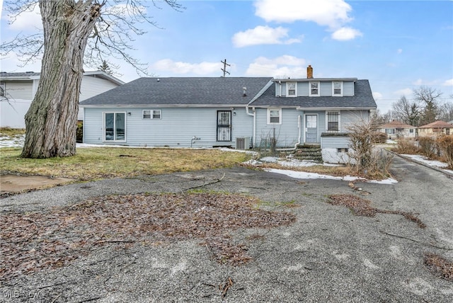 rear view of property with driveway, a shingled roof, a chimney, and cooling unit