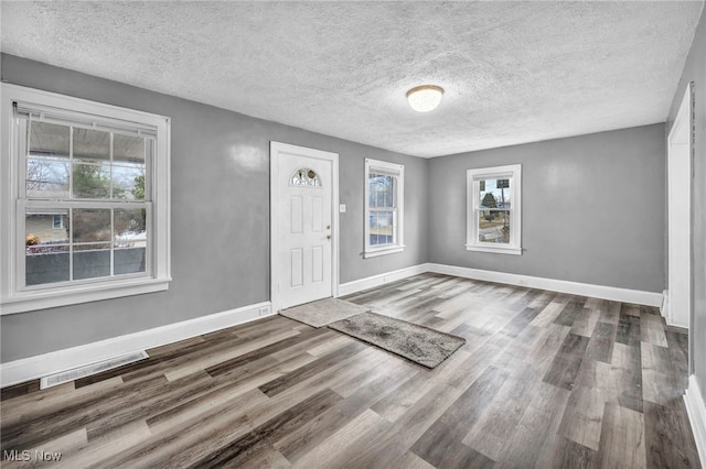 foyer featuring visible vents, a textured ceiling, baseboards, and wood finished floors