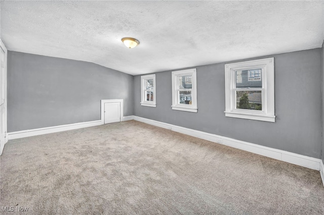 carpeted empty room with lofted ceiling, a textured ceiling, and baseboards