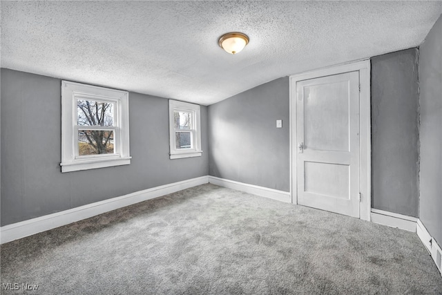 unfurnished room with carpet floors, lofted ceiling, a textured ceiling, and baseboards