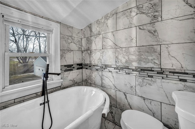 full bath with a freestanding bath, a textured ceiling, and toilet