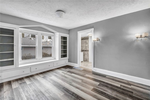 spare room featuring a textured ceiling, wood finished floors, visible vents, and baseboards