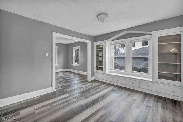 empty room with a textured ceiling, baseboards, and wood finished floors