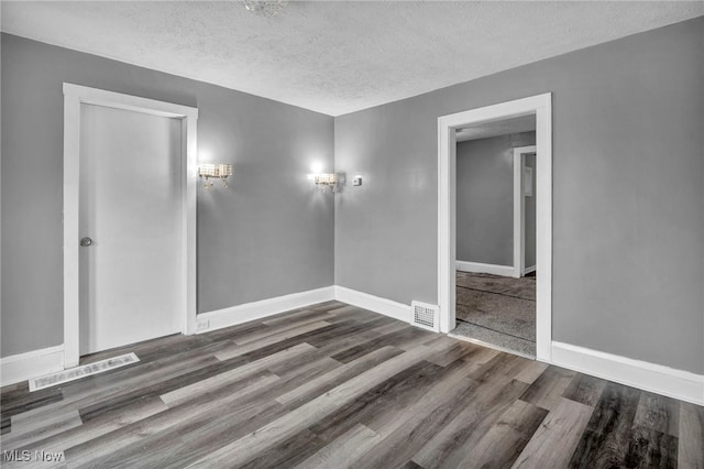 spare room featuring visible vents, a textured ceiling, baseboards, and wood finished floors