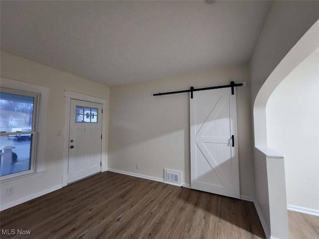 entrance foyer featuring a barn door, wood finished floors, visible vents, and baseboards