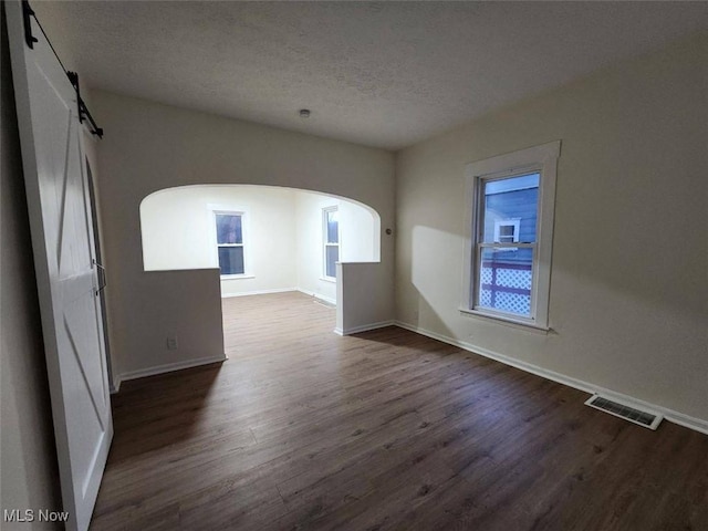 unfurnished room with arched walkways, dark wood finished floors, visible vents, a barn door, and a textured ceiling