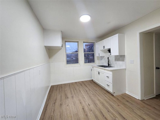 kitchen with light wood finished floors, a wainscoted wall, light countertops, white cabinetry, and a sink