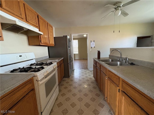 kitchen featuring brown cabinetry, a sink, ceiling fan, white range with gas stovetop, and under cabinet range hood