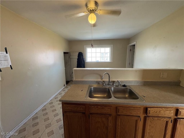 kitchen with ceiling fan, a sink, baseboards, light floors, and brown cabinetry